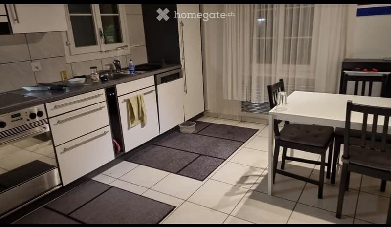 Modern kitchen with white cabinets, stainless steel appliances, a dining table with chairs, and a curtained window.