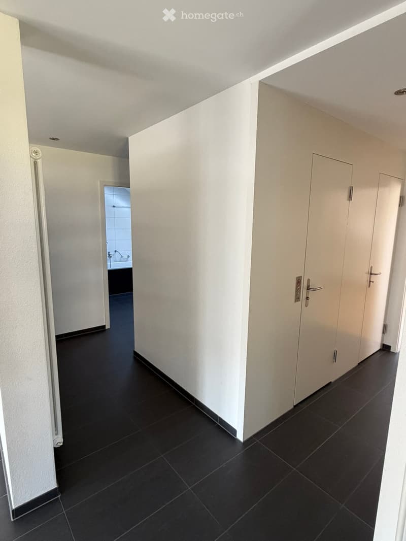 Clean, modern hallway with white walls, black tiled floor, and several closed doors. A small bathroom is visible at the end of the hallway.