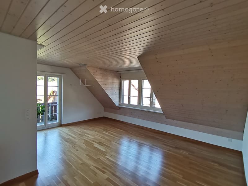 Empty attic space with wooden ceiling, wooden floor, and large windows, featuring a sliding glass door leading to a balcony.