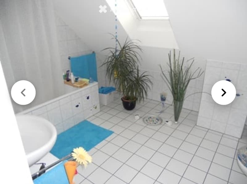Bathroom with white tiled floor and walls, a sink, a bathtub, a potted plant, and a vase with a flower on the floor.