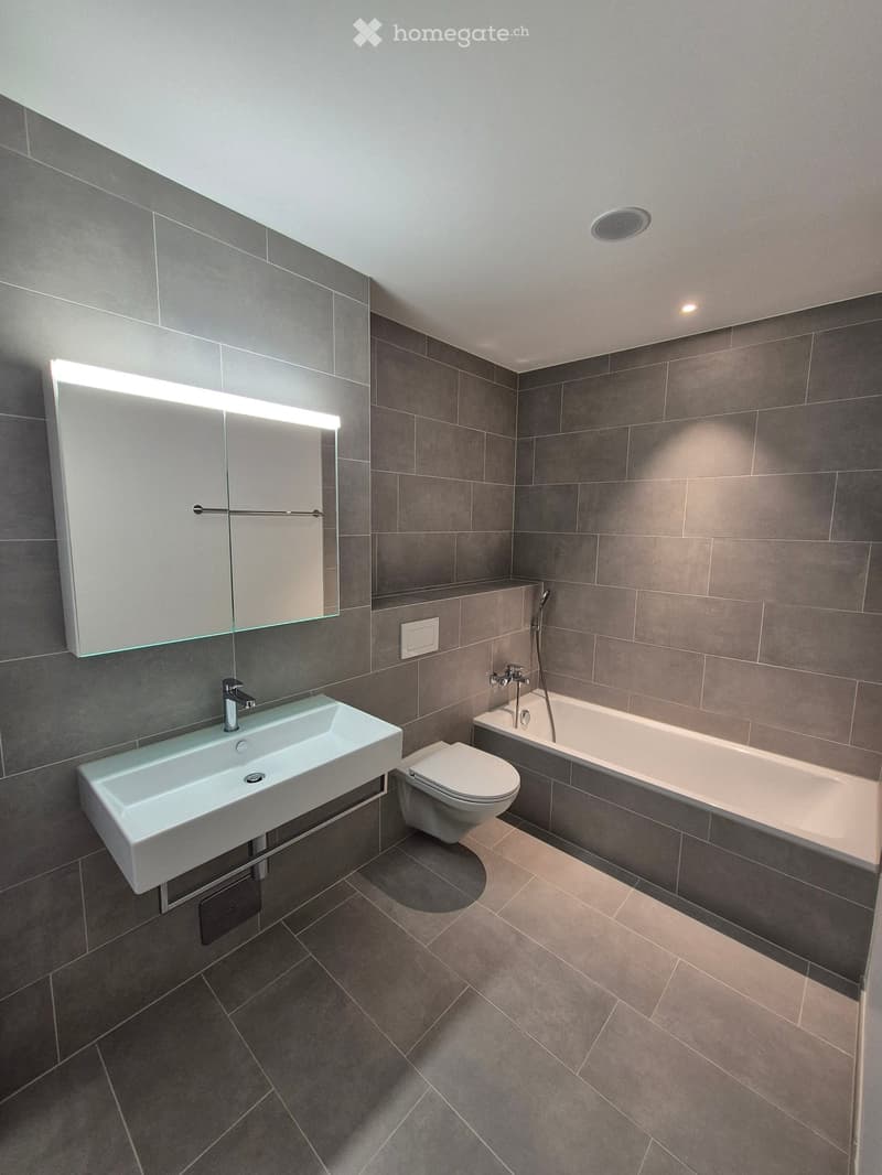 Bathroom: white tiles, large mirror, sink, toilet, bathtub, faucet