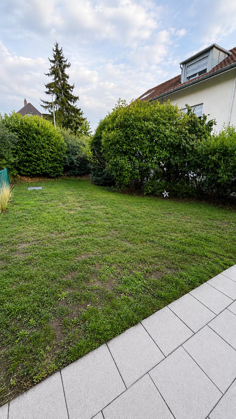 Well-maintained garden with green lawn, shrubs, and a raised garden bed bordered by patterned concrete tiles.