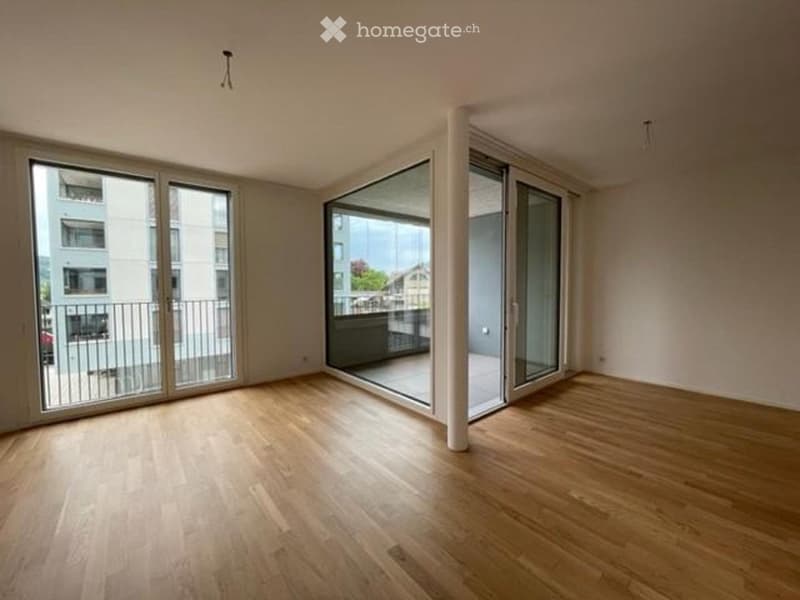 Empty room with wooden flooring, large sliding glass doors leading to a balcony, and white walls.
