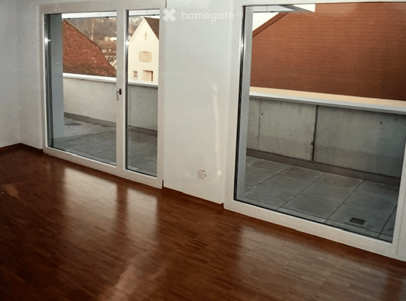 Empty room with wooden flooring, large sliding glass doors leading to a balcony, and white walls.