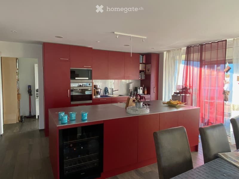 Modern kitchen with red cabinets, central island, built-in oven, sink, and seating area with chairs and table.