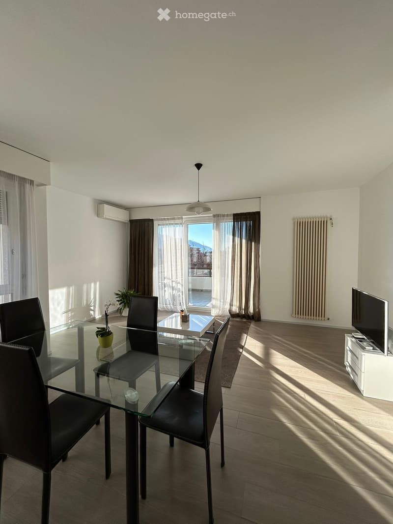 Modern dining area with a glass table, black chairs, TV, and large windows with curtains.