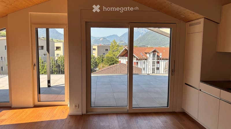 Bright room with wooden flooring, large sliding glass doors leading to a balcony with a scenic mountain view, and white cabinets.