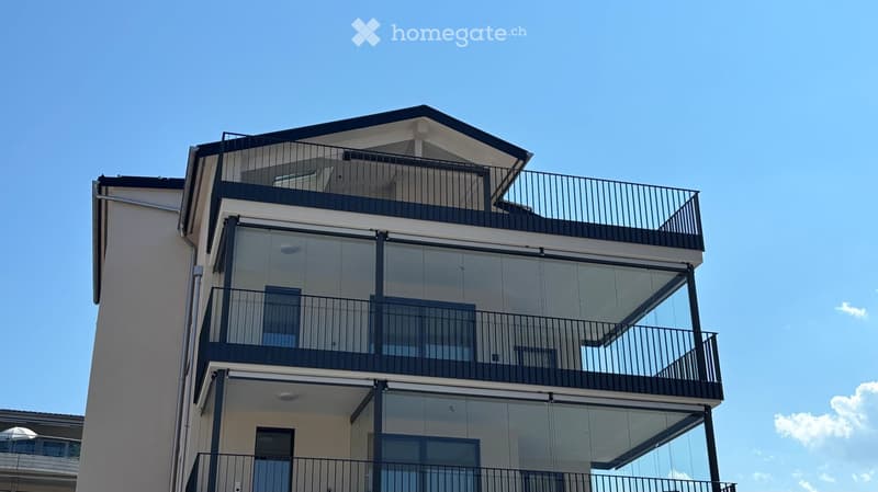 Modern multi-story residential building with balconies and glass railings, featuring a flat roof and contemporary design.