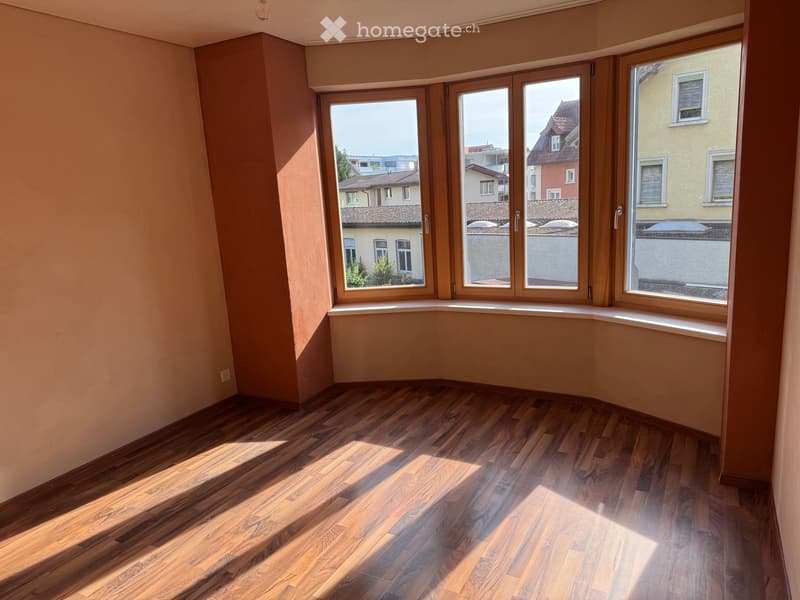 Empty room with wooden flooring and large windows offering a view of the cityscape.