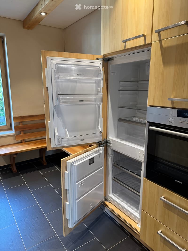 Modern kitchen with light wooden cabinets, a built-in refrigerator, and an oven. The refrigerator doors are open, revealing empty shelves.