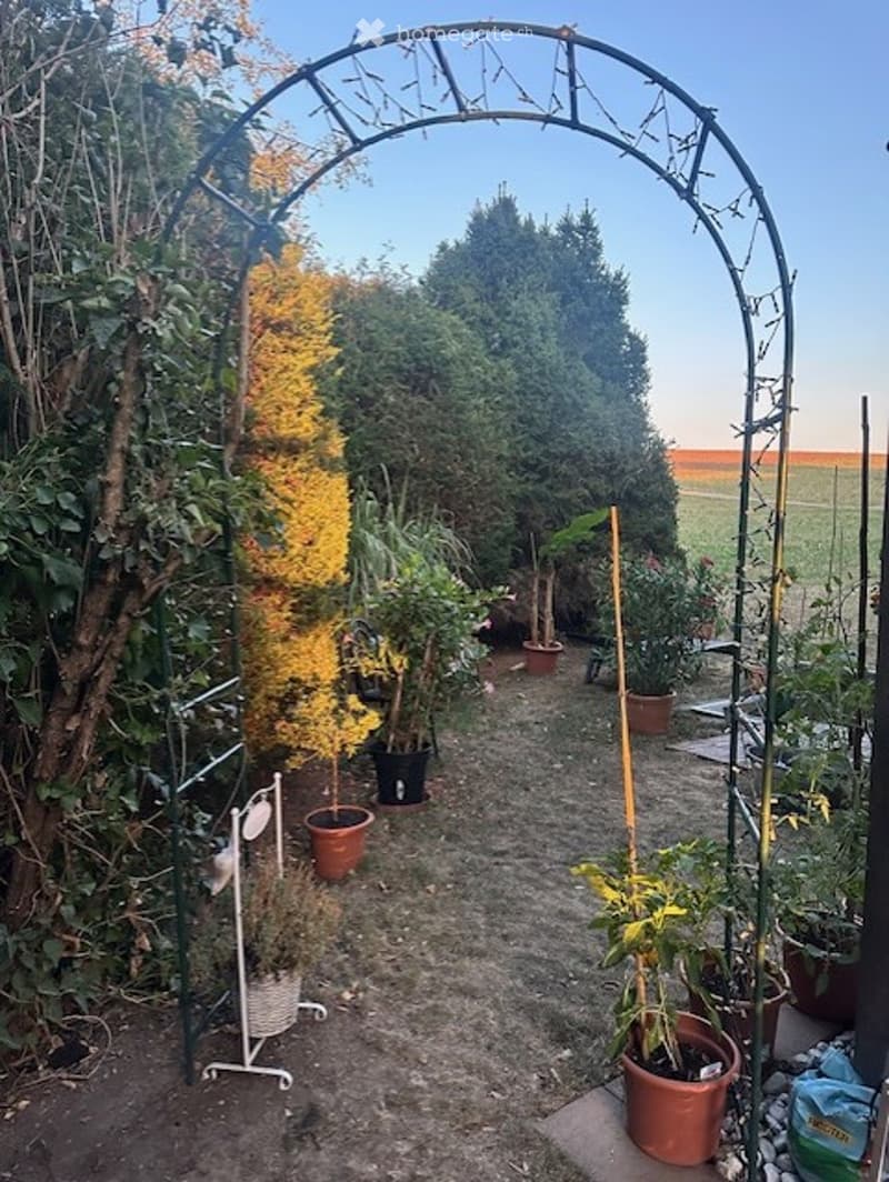 Garden area with potted plants, a metal archway, and a gravel pathway.