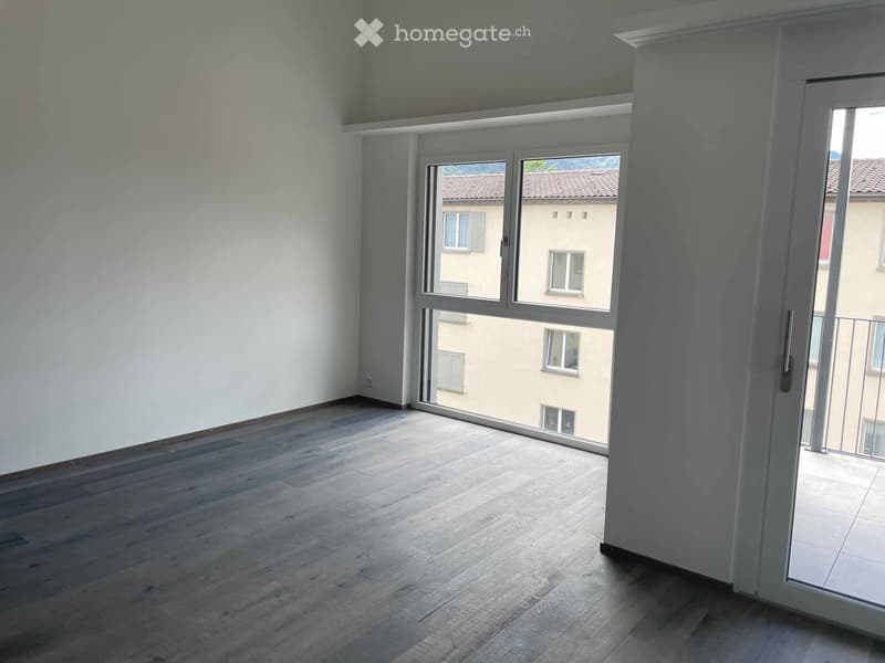 Empty room with wooden flooring, large windows, and white walls. No furniture or equipment present.
