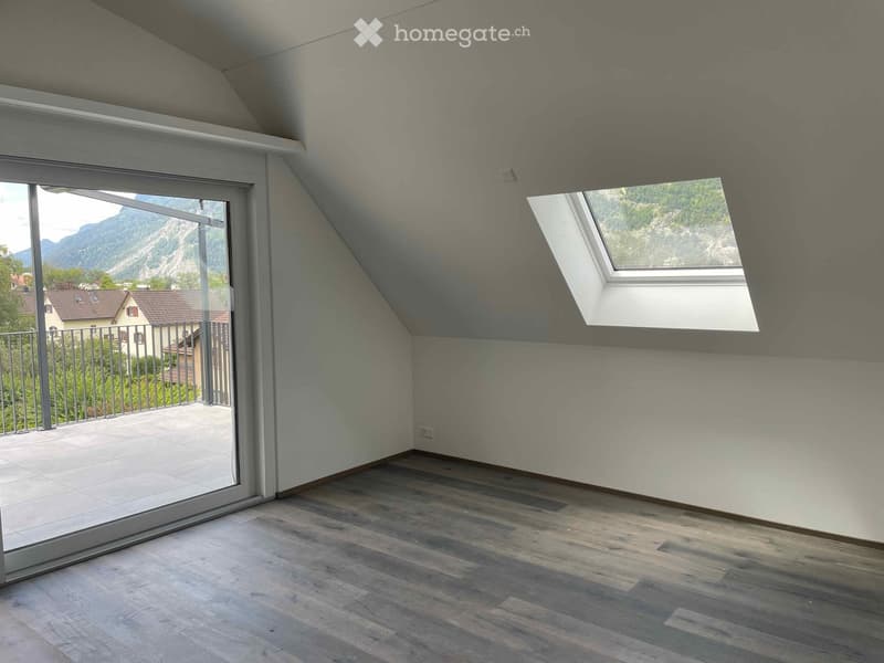 Empty attic room with wooden flooring, large skylight window, and sliding glass door leading to a balcony with a scenic mountain view.
