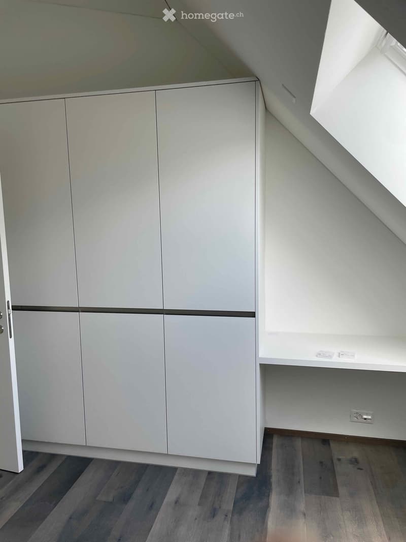Empty room with light grey cabinets, white shelving, and wooden flooring.