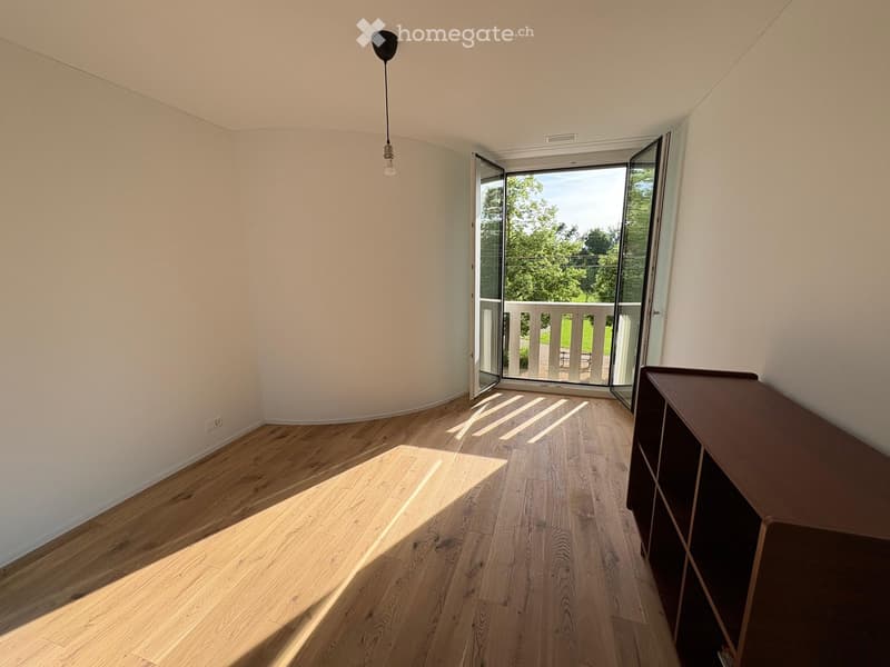 Empty room with wooden flooring, white walls, and a single cabinet. Large sliding glass doors open to a balcony with outdoor furniture visible.