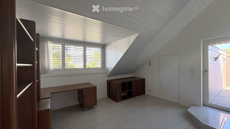 Bright, modern room with slanted ceiling, large windows, and built-in wooden furniture including a desk and cabinet.