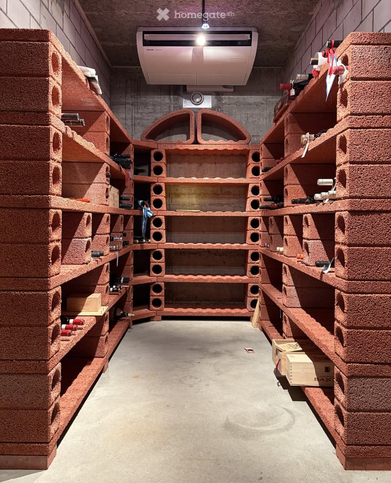 Wine cellar with brick wine racks, shelves filled with wine bottles, and wooden crates on the floor.