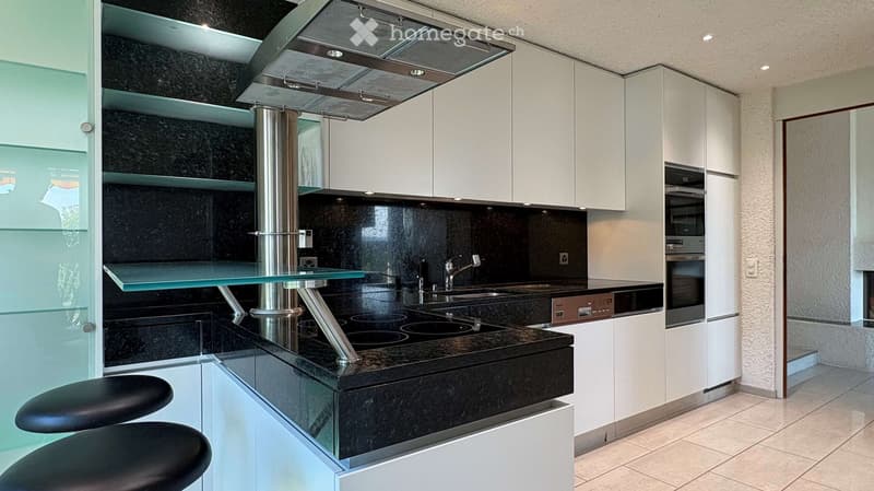 Modern kitchen with white cabinets, black granite countertops, built-in stove, sink, and stools.