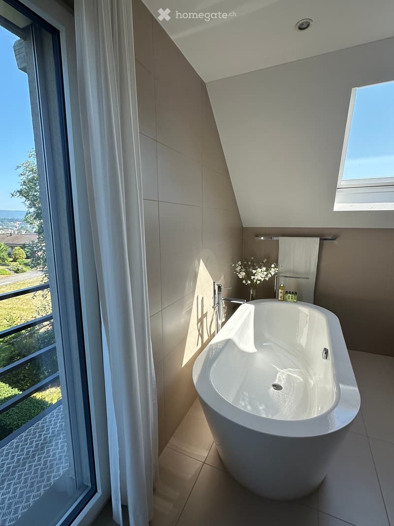 Modern bathroom with a large bathtub, sleek faucet, and a scenic view through a large window.