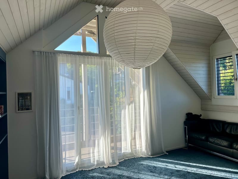 Bright living room with a large window and sliding glass door, white curtains, a black leather sofa, a large round pendant light, and a picture frame on the wall.