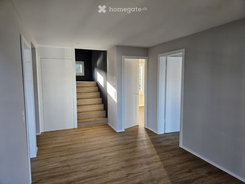 Empty hallway with wooden flooring, white walls, and a staircase leading upwards.