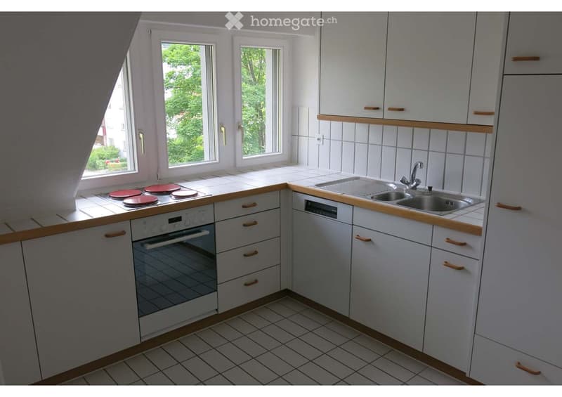 Modern kitchen with white cabinets, wooden countertops, and stainless steel appliances including an oven, sink, and dishwasher. The kitchen features three windows with a view of greenery outside.
