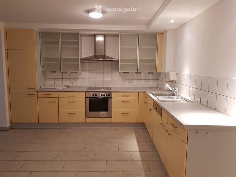 Modern kitchen with light yellow cabinets, stainless steel appliances, tiled backsplash, and a central island.