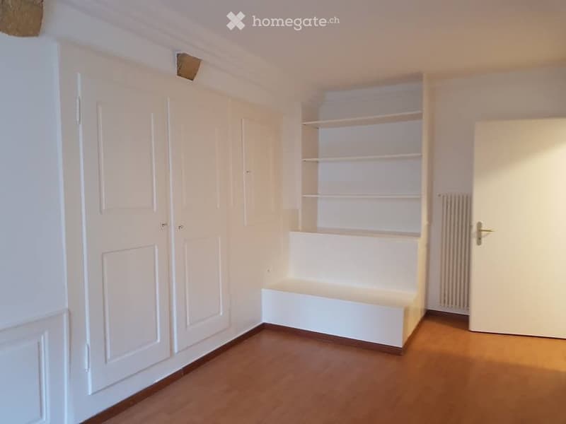 Empty room with white walls, wooden flooring, built-in white shelving unit, and a small bench with integrated lighting.