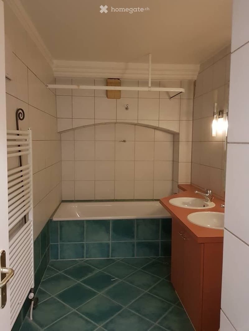 Bathroom with a bathtub, two sinks, a towel rack, and a cabinet. The walls are tiled, and the floor is green tiled.