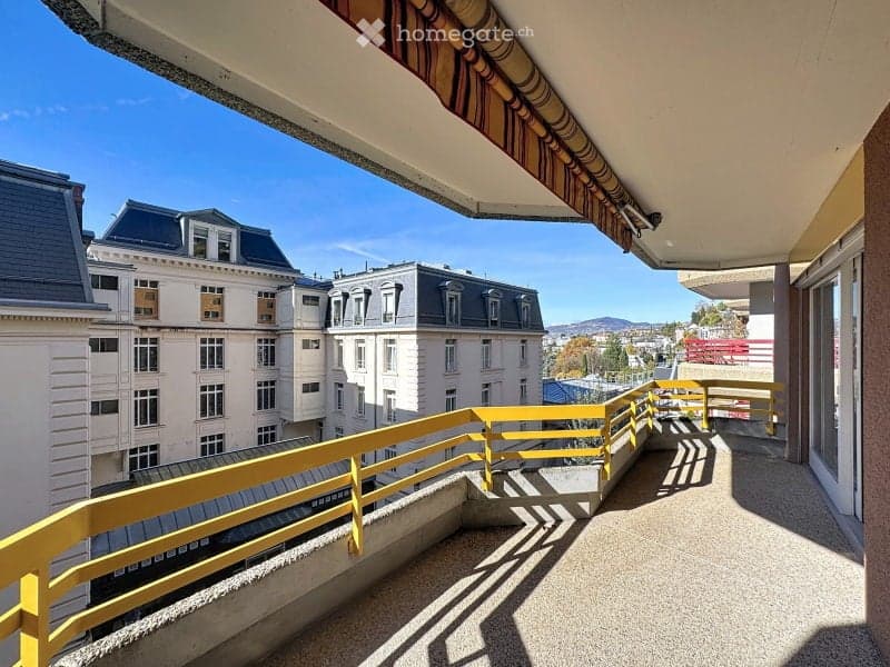 Balcony with yellow railing, overlooking a cityscape with classic buildings and distant mountains.