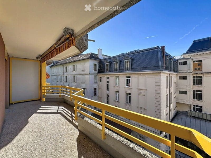 Balcony with yellow railing, overlooking a cityscape of classic European buildings with grey roofs and white facades.