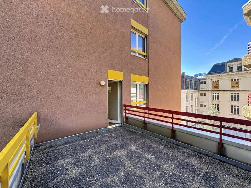 Balcony with a red metal railing, concrete floor, and access door to the building.