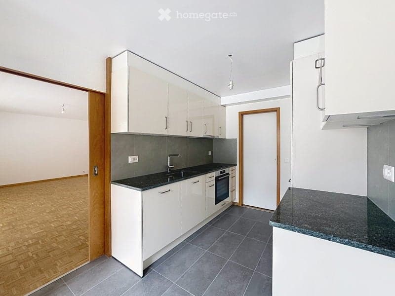 Modern kitchen with white cabinets, dark countertops, and grey tiled floor. Features a sink, oven, and faucet.