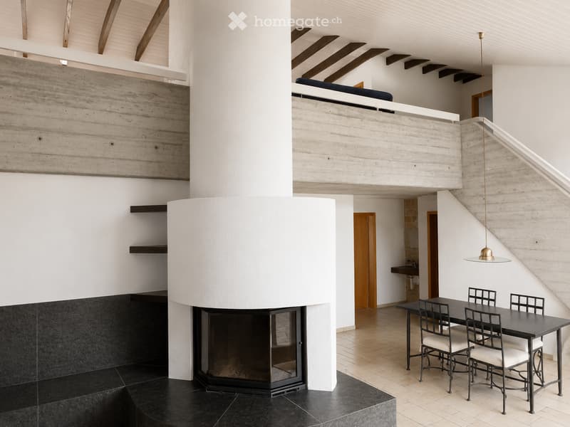 Modern open-plan living and dining area with a central fireplace, a dining table with chairs, and a hanging lamp.