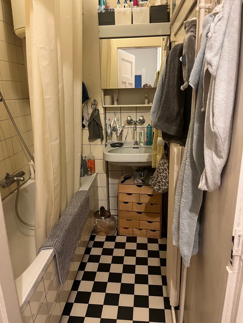 A small bathroom with a black and white checkered floor, a sink with a mirror above it, a bathtub with a shower curtain, and various toiletries and towels visible.
