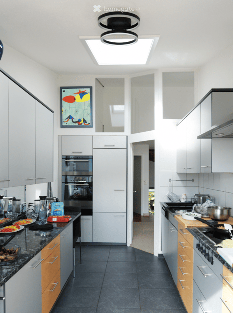 Modern kitchen with white cabinets, stainless steel appliances, granite countertops, and a skylight above the island.