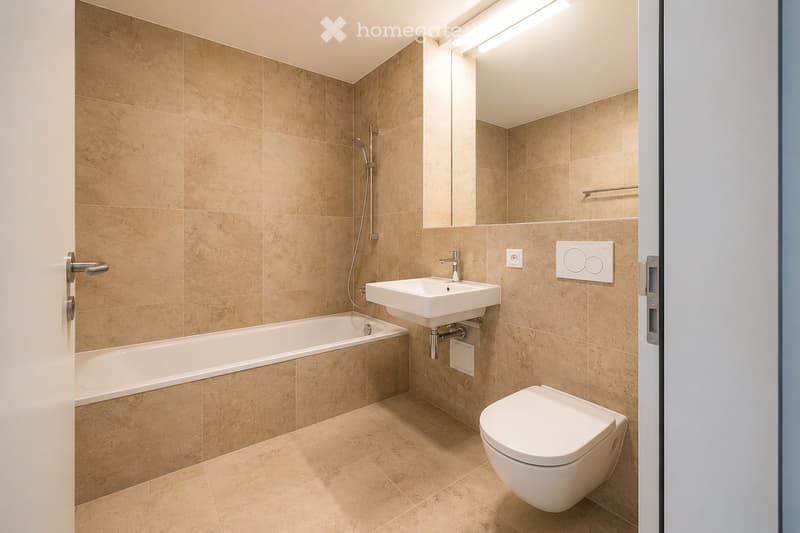 Modern bathroom with beige tiled walls and floor, featuring a bathtub, toilet, sink, and showerhead.