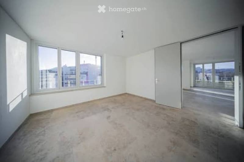Empty room with white walls, large windows, and a sliding door leading to a balcony area.