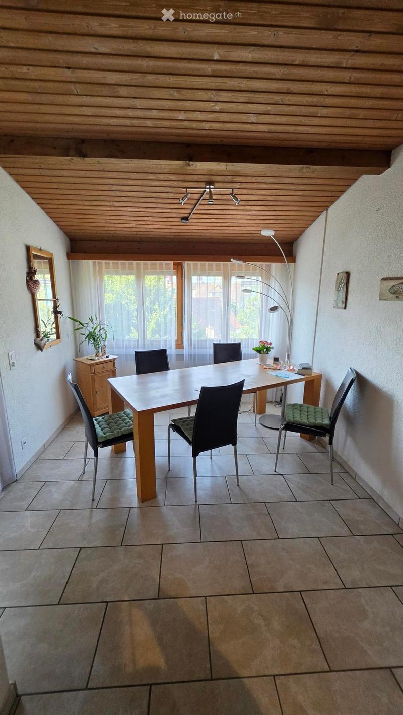 Dining room with a wooden dining table, four chairs, a floor lamp, a sideboard, and a small plant on the windowsill.