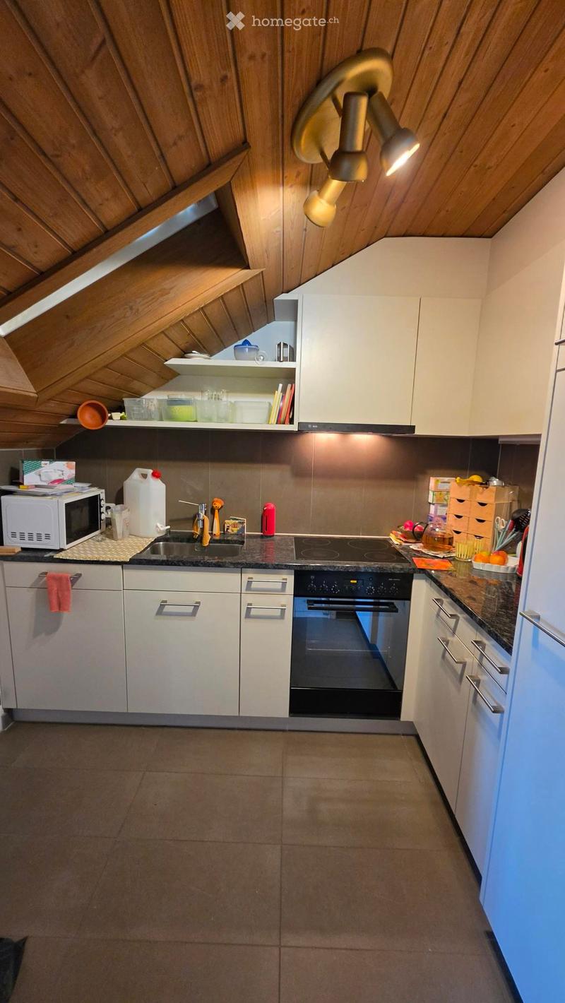 Modern kitchen with white cabinets, dark countertops, and stainless steel appliances including a microwave, oven, and sink. Wooden ceiling with built-in lighting.