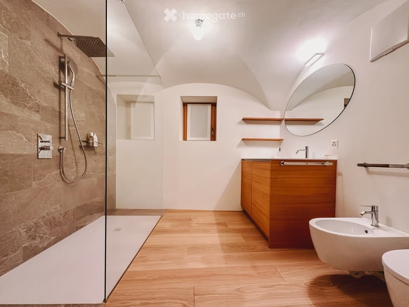 Bathroom. Modern bathroom with wooden flooring, a large oval mirror, a wooden vanity cabinet, a shower area with glass enclosure, and a toilet.