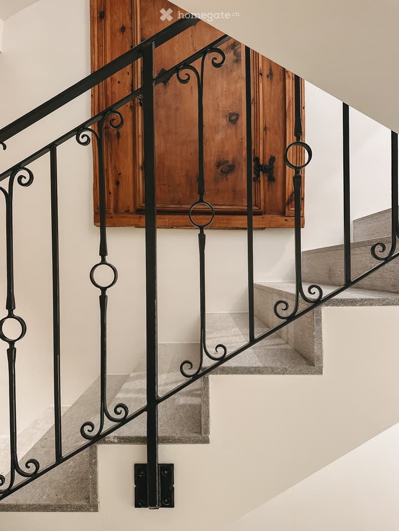 Corridor / Hallway. Staircase with black wrought iron railing and wooden door in the background.