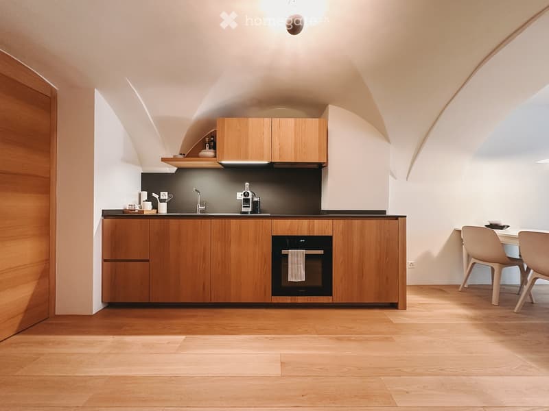 Kitchen. Modern kitchen with wooden cabinets, stainless steel sink, built-in oven, and a small dining area with chairs and table.