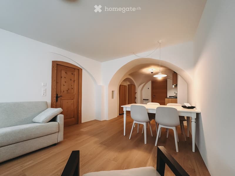Furnished Room. Modern living and dining area with light-colored furniture, wooden flooring, and arched doorways leading to a kitchen area.