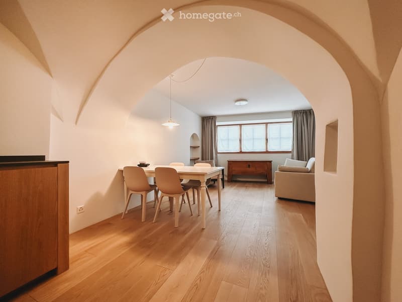 Furnished Room. Open-plan living and dining area with wooden flooring, a sofa, a dining table with chairs, and a wooden cabinet.