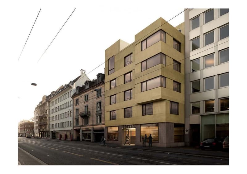 Modern multi-story building with large windows and a contemporary design, located on a city street with other buildings and traffic visible.