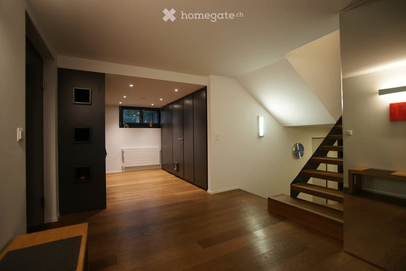 wooden floor, white walls, black cabinets, radiator, staircase, wall clock, wall mounted light