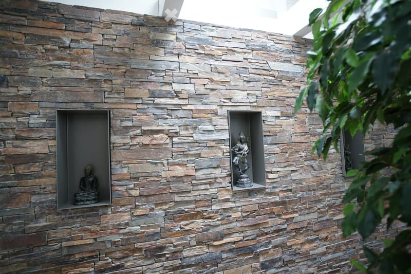 Stone wall with three niches containing statues, a plant on the right side