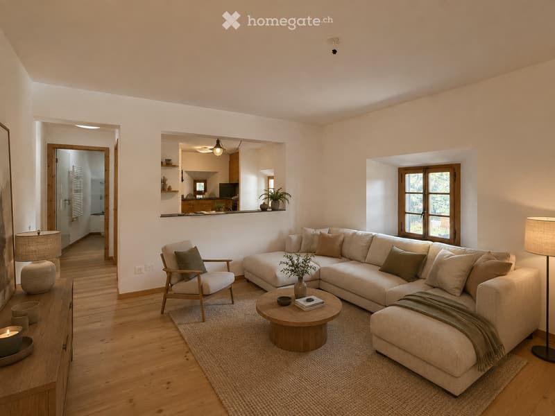 Modern living room with light-colored sofa, coffee table, armchair, floor lamp, and decorative items. Open-plan layout with visible kitchen area in the background.