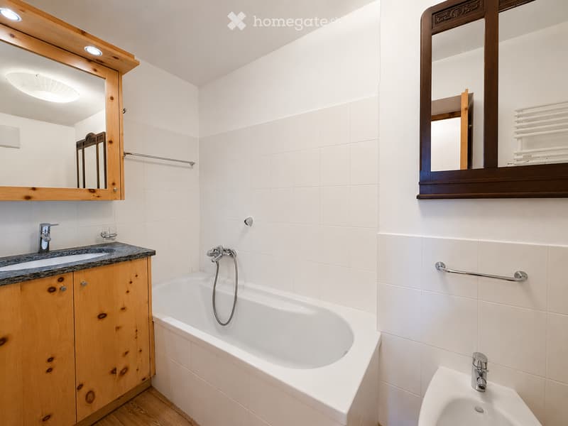 Modern bathroom with white tiles, a bathtub, a sink with a wooden cabinet, and two mirrors with wooden frames. Includes a towel rack and a bidet.